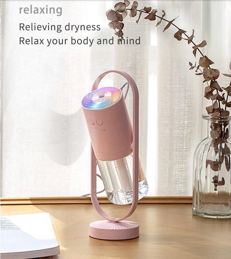 Pink USB air humidifier with cylindrical water tank and projection night light on wooden surface.